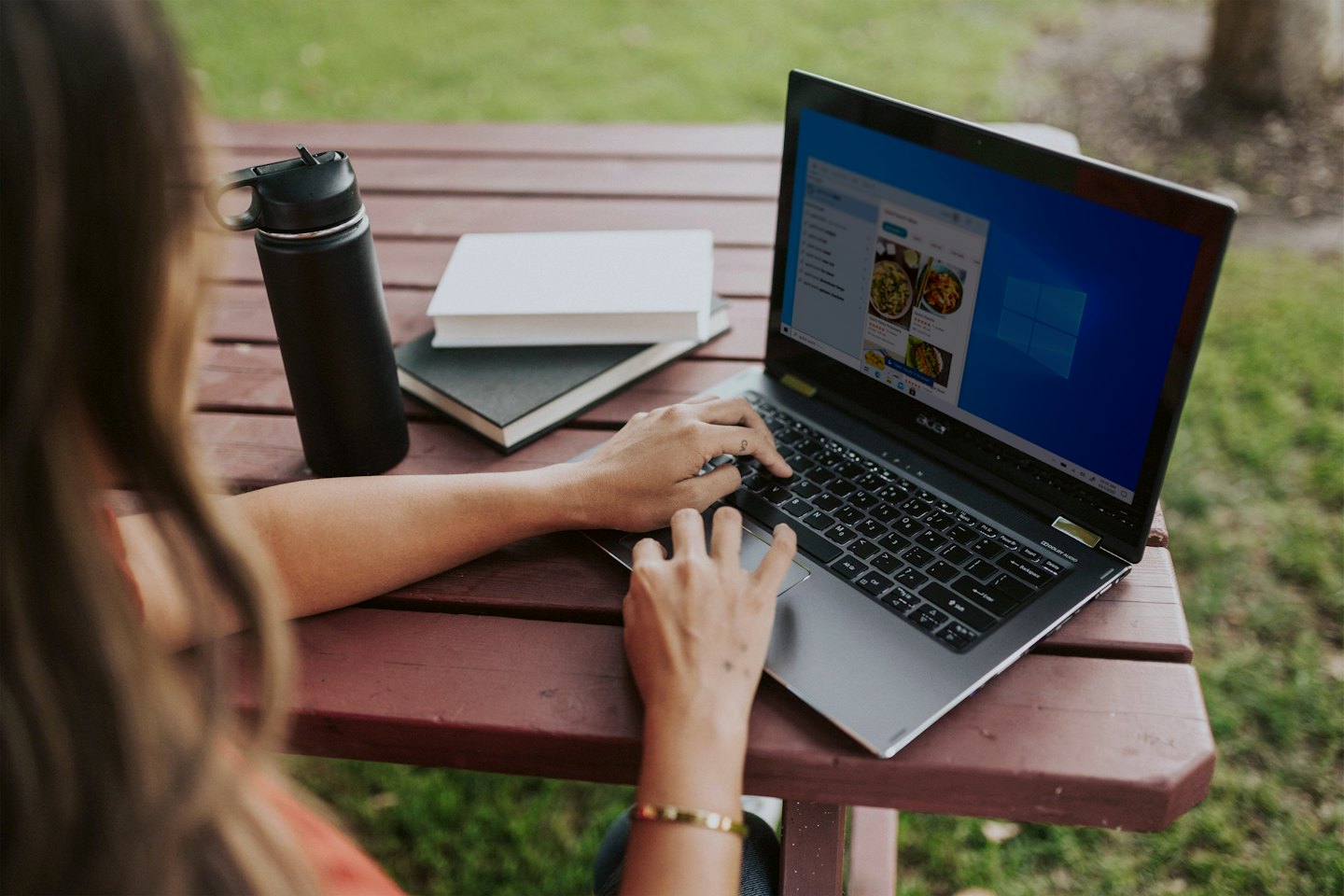Person typing on a laptop at a wooden picnic table.